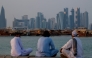 People sit along the corniche facing traditional dhow boats anchored in front of the Doha skyline on October 29, 2025. (Photo by Karim Jaafar / AFP)