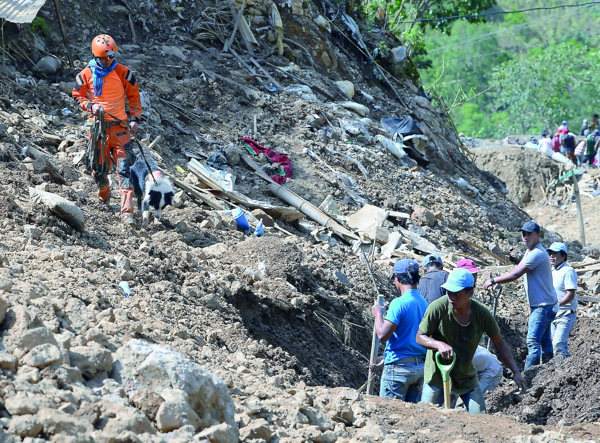 A rescuer guides his sniffer dog while volunteers recuers search for landslide victims, triggered by heavy rains during Typhoon Mangkhut, in Itogon, Benguet province on September 18, 2018. AFP / Ted Aljibe