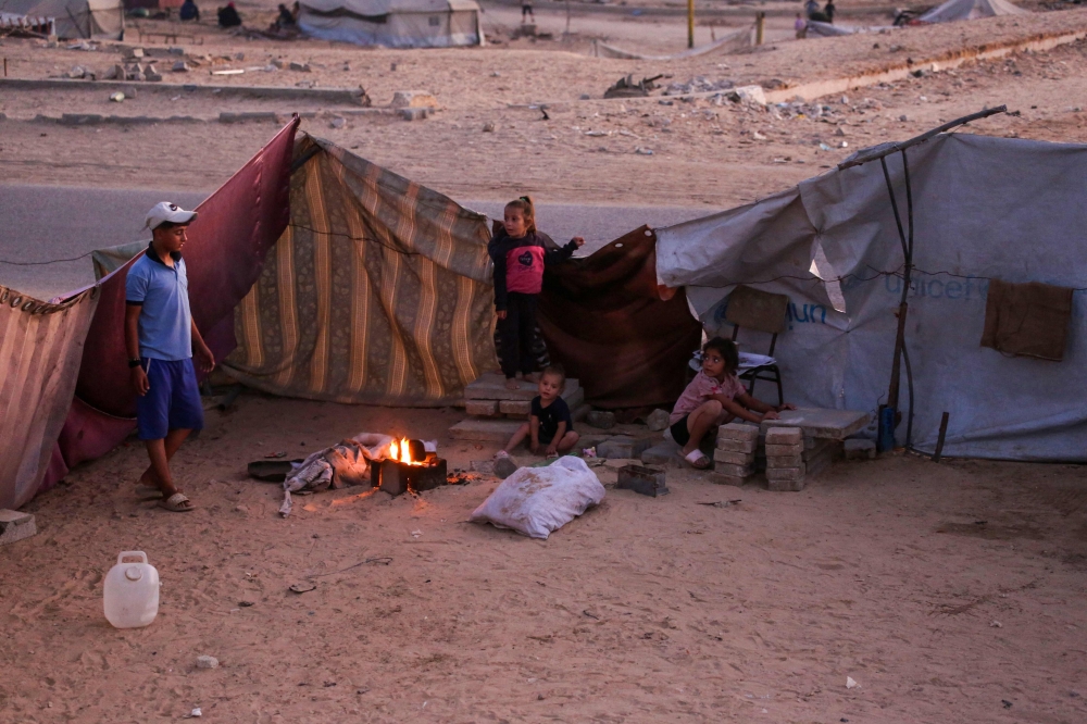 Palestinians sit by the fire in their makeshift shelter in Khan Yunis, in the southern Gaza Strip on October 25, 2025. (Photo by Bashar Taleb / AFP)