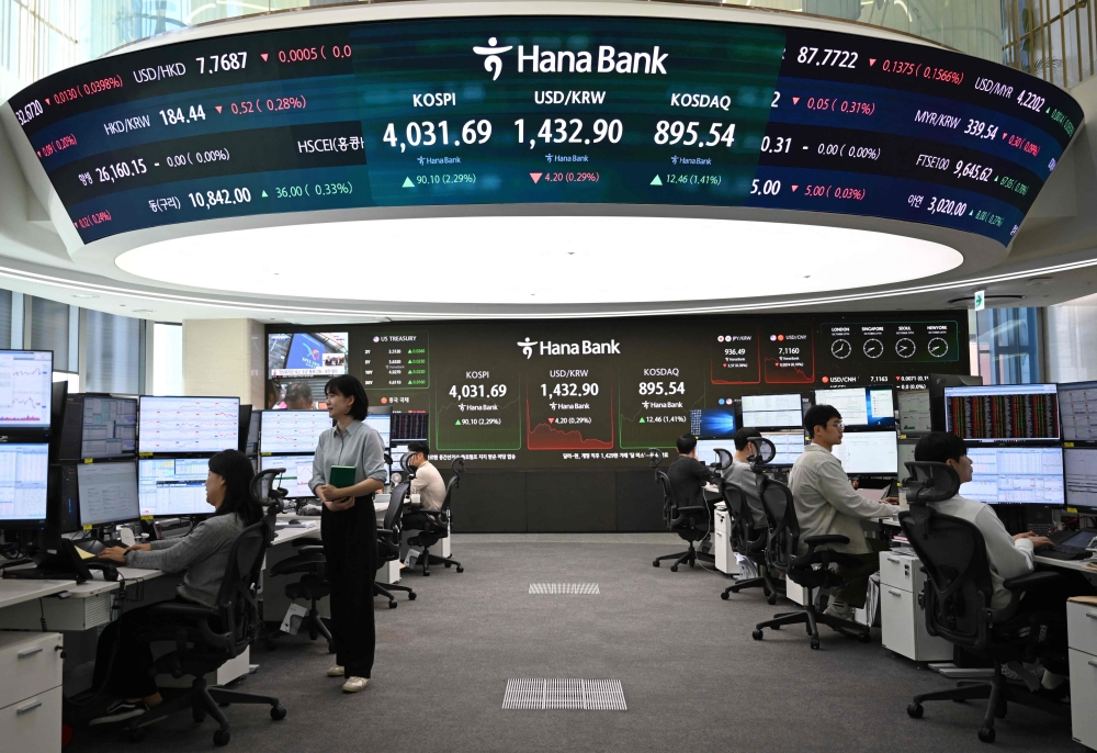 Currency dealers monitor exchange rates in front of a screen showing South Korea's benchmark stock index and the Korean won/USD exchange rate in a foreign exchange dealing room at the Hana Bank headquarters in Seoul on October 27, 2025. (Photo by Jung Yeon-je / AFP)